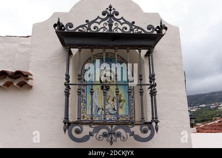 Eine alte Ikone hängt an der Außenwand des Hauses hinter einem schönen schmiedeeisernen Zaun auf der Insel Teneriffa in Spanien. Stockfoto