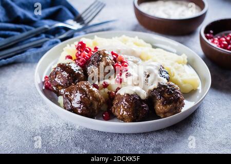 Hausgemachte Fleischbällchen aus Rind und Schwein mit Kartoffelpüree und Preiselbeersoße auf einem grauen Steinbeton-Hintergrund. Mittagessen Abendessen Essen Konzept Stockfoto