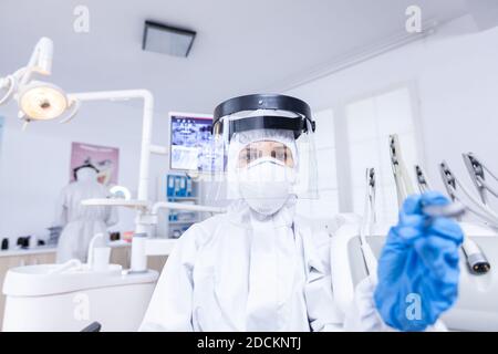 Patient pov während Zahnarzt in Schutzanzug für covid arbeitet an Zahn hygine. Stomatolog trägt Sicherheitsausrüstung gegen Coronavirus während der Hitzebehandlung des Patienten. Stockfoto