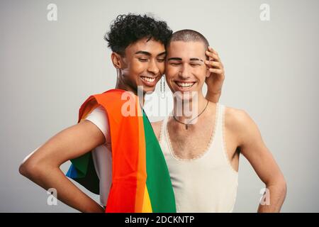 Fröhliche Homosexuell Paar mit Stolz Flagge auf weißem Hintergrund. Zwei homosexuelle Männer stehen zusammen und lächeln. Stockfoto