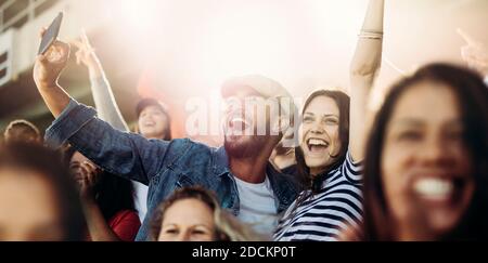 Ein Paar, das Selfie beim Jubeln im Stadion nimmt. Aufgeregt Männer und Frauen Fans nehmen Selfie während der Wiedergabe Spiel im Stadion. Stockfoto