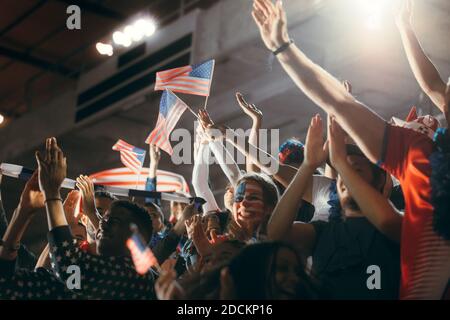 Fußballfans im Stadion mit Gesicht in den USA-Flaggenfarben und schwenkenden Fahnen. Fußballfans aus amerika in der Fanzone sehen sich ein Spiel an. Stockfoto