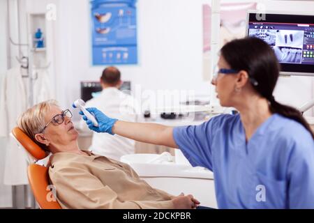 Zahnarzthelferin Messung Senior Frau Körpertemperatur mit Thermometer während der Konsultation. Medizinische Facharzt in der Zahnklinik unter Patienten Temperatur mit digitalen Gerät. Stockfoto