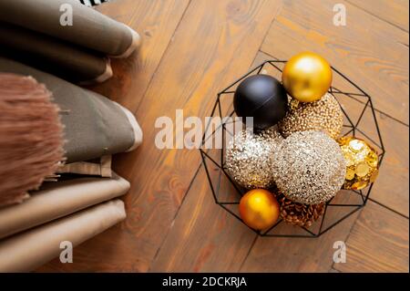 Goldene, beige und schwarze glänzende Kugeln für Weihnachtsdekor in einem schwarzen Metallkorb auf einem Holzdeckel. Weihnachtskarte, selektiver Fokus Stockfoto