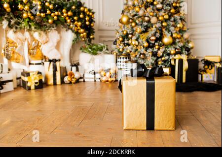 Gold Geschenkbox mit schwarzem Band auf Holzboden im Zimmer mit Weihnachtsdekor in Gold und schwarzen Farben : Weihnachtsbaum mit Kugeln und Girlanden und Mann Stockfoto