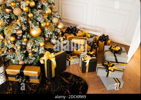 Viele Geschenkschachteln in Geschenkpapier und Bänder in schwarz und Gold unter großen flauschigen Weihnachtsbaum mit Girlande, Weihnachtskarte, selektive Focu Stockfoto