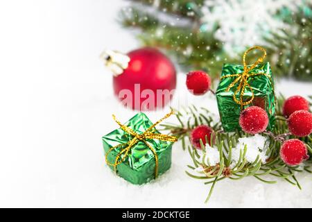 Weihnachtskarte mit einem grünen Zweig eines Weihnachtsbaums mit Geschenken und roten runden Spielzeugen auf weißem Hintergrund. Zusammensetzung der Weihnachtsferien. Stockfoto