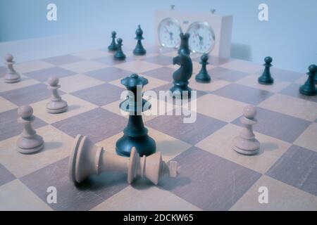 Weißer König und schwarze Königin in einem Schachspiel. White ist zurückgetreten und hat seinen König flach auf das Schachbrett gelegt. Stockfoto