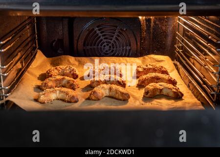 Frisch gebackene leckere vegane Mandelcroissants mit gehackten Mandeln auf einem Backblech in einem beleuchteten Ofen. Es ist ein schmackhaftes Makronen-Gebäck mit Marzipan. Stockfoto