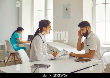 Medizinische Klinik. Frau Arzt hören zu zeigen Kopfschmerzen Mann Patient und Notizen Stockfoto