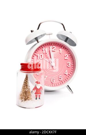 Festlicher Wecker, der eine Minute vor Mitternacht neben einem Weihnachtsschmuck mit Weihnachtsmann und einem Weihnachtsbaum mit Schnee, isoliert auf Weiß, zeigt. Stockfoto