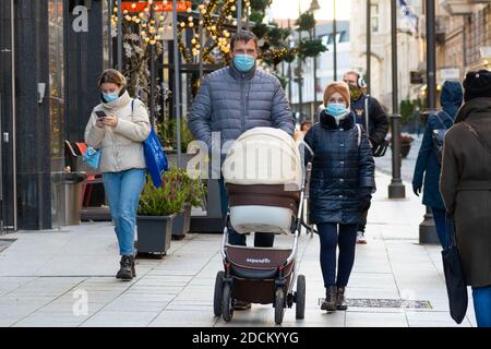 Paar mit Kinderwagen und Menschen mit Schutzmaske zu Fuß in der Stadt in der Nähe eines Geschäfts oder Einkaufszentrum während Weihnachten, Covid oder Corona Stockfoto