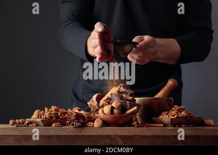 Der Mann streut die Schokolade mit Kakaopulver. Auf einem alten Holztisch Süßigkeiten, Zutaten und Stücke von gebrochener schwarzer Schokolade. Speicherplatz kopieren. Stockfoto