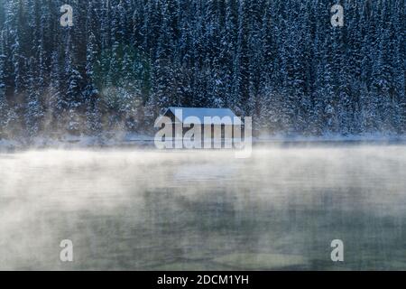 Lake Louise Bootshaus in frühen Winter sonnigen Tag Morgen. Nebel schwimmt auf türkisfarbener Wasseroberfläche. Banff National Park. Stockfoto