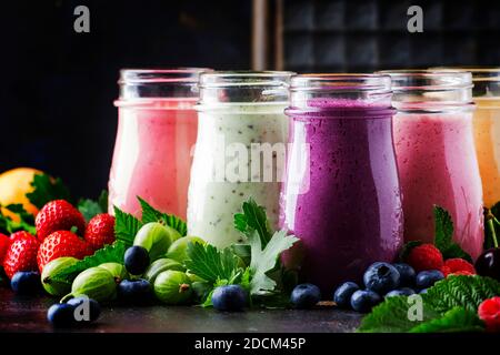 Gesunde und nützliche bunte Beere cokctalis, Smoothies und Milchshakes mit Joghurt, frischem Obst und Beeren auf braunem Tisch, selektiver Fokus Stockfoto