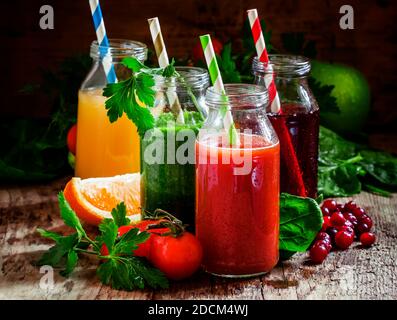 Mix aus gesunden Obst- und Gemüsesäften in kleinen Flaschen mit farbig gestreiften Trinkhalmen, altem Holzhintergrund, selektiver Fokus Stockfoto