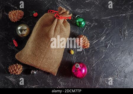 Weihnachtstasche aus grobem Sackleinen, Zapfen, Weihnachtsschmuck, auf dunklem Hintergrund Platz für Text. Speicherplatz kopieren. Stockfoto