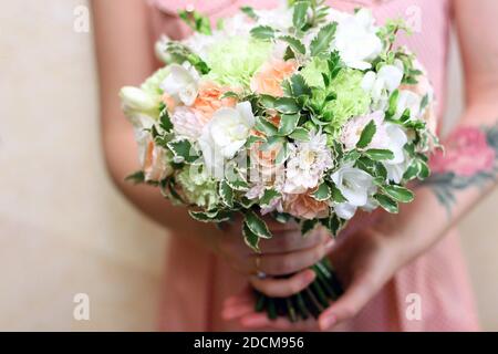 Rundes weiß-grünes Bouquet in weiblichen Händen. Die junge Frau hat ein Tattoo am Arm, sie ist in einem rosa Kleid. Das Bouquet ist frisch, schön und Stockfoto