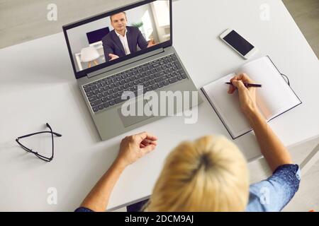 Ältere Frau, die sich beim Videoanruf mit einem Kollegen Notizen gemacht hat Oder dem Business Lecturer zuhören Stockfoto