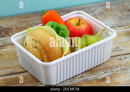 Nahrhafte Lunchbox mit braunem Käse-Sandwich, knusprigem gelben Pfeffer und frischem Obst in weißer Plastikbox Stockfoto