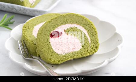 Köstliche Matcha Swiss Roll Cake Scheiben mit Erdbeer-Pudercreme auf weißem Hintergrund, Nahaufnahme. Stockfoto