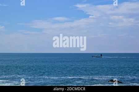 Blick auf das Meer und ein entferntes Motorboot, das sich gerade bewegt Unter der Linie des Horizonts auf einem teilweise bewölkten Tag im Spätsommer Stockfoto