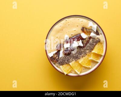 Dekoriertes Frühstück Smoothie Schüssel mit Banane und Orange auf gelbem Hintergrund, Blick von oben Stockfoto