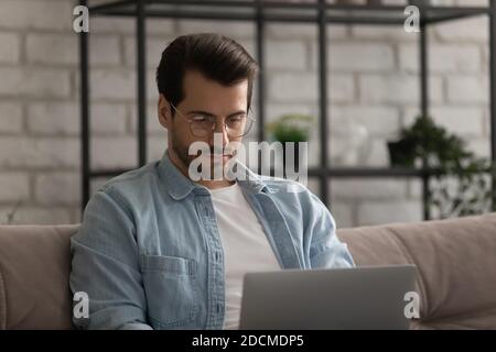 Fokussierter junger Mann mit Brille, der entfernt am Computer arbeitet. Stockfoto