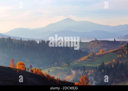 Atemberaubende Herbstlandschaft. Landschaft mit hohen Bergen, Feldern und Wäldern bedeckt mit Morgennebel. Der Rasen wird von den Sonnenstrahlen erleuchtet. Touristisch Stockfoto