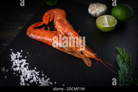 Zwei große Langusten mit Limette, Salz, Knoblauch und Kräutern auf einem schwarzen Teller. Meeresfrüchte gesund. Stockfoto