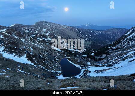 Nachtlandschaften. See an den hohen Bergen. Der Mond erleuchtet das Tal. Schneebedeckte Wiesen. Lage Ort der Karpaten, Ukraine, Europa. Stockfoto