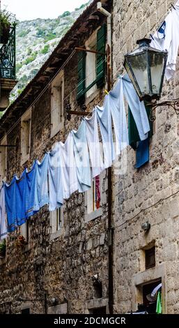 Wäscheleine mit Handtüchern, die draußen von einem alten Steinhaus in einer Reihe von Farben von weiß bis blau hängen. Aufgenommen in der Altstadt von Kotor, Montenegro Stockfoto