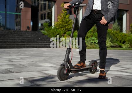 Bequemer Transport. Eine kurze Aufnahme eines eleganten, stilvollen Geschäftsmanns mittleren Alters, der tagsüber mit seinem Elektroroller auf der Stadtstraße steht Stockfoto