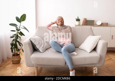 In voller Länge Porträt der schwarzen Frau in Hijab ruht auf Bequeme Couch zu Hause Stockfoto