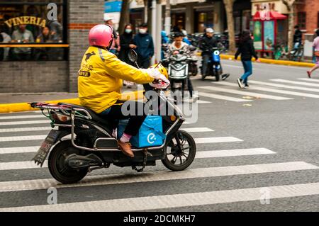 Ein Mitituan-Lieferer auf einem Roller mit einer Eleme-Liefertasche an der Kreuzung von Jiaozhou und Wuding Straßen im Jing’an Bezirk in Shanghai. Stockfoto