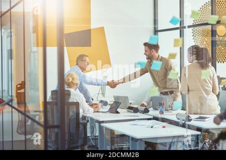Gutes Angebot. Zwei Geschäftsleute oder Kollegen, die sich die Hände schütteln, während sie sich mit Kollegen im modernen Büro treffen Stockfoto
