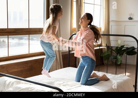 Fröhliches kleines Mädchen halten Mama Hände springen auf Bett Stockfoto