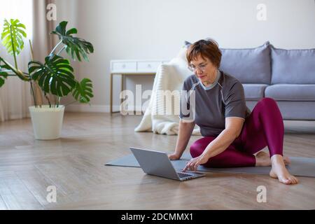 Ältere Frau mit Kopfhörern bereitet sich auf das Training im Internet vor. Sie sucht im Internet nach Übungsvideos. Stockfoto