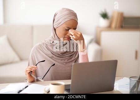 Müde schwarze Frau in Hijab reiben ihre Augen während der Arbeit Online auf dem Laptop zu Hause Stockfoto