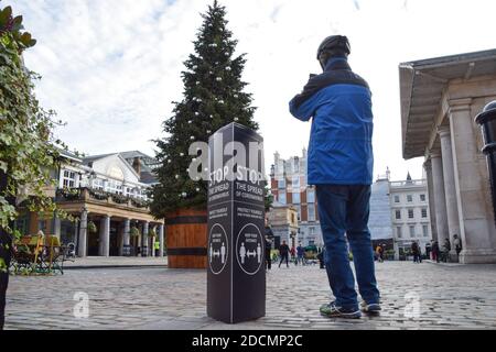 Ein Mann macht ein Foto vom Weihnachtsbaum neben dem Schild Stop the Ausbreitung des Coronavirus in Covent Garden, London. England wird ein hartes Tier-System durchsetzen, sobald die Sperre am 2. Dezember endet. Stockfoto