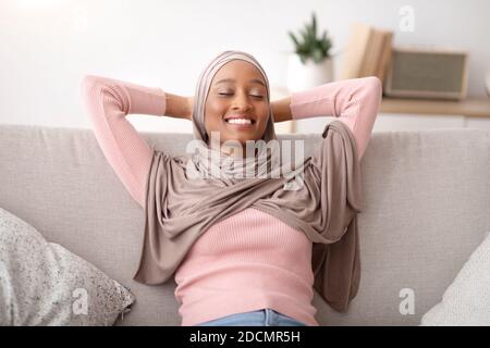 Schöne muslimische Frau in traditionellen Hijab entspannen auf dem Sofa mit geschlossenen Augen, drinnen Stockfoto