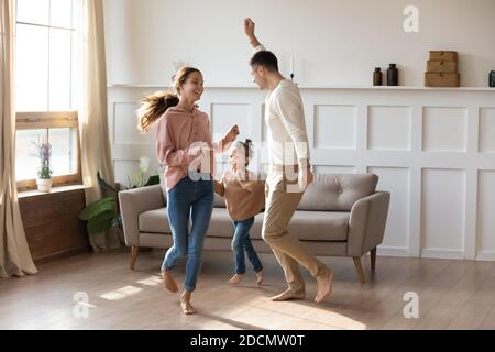 Pärchen tanzt mit kleiner Tochter barfuß im warmen Wohnzimmer Stockfoto