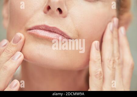 Gepflegte Lippen der kaukasischen Frau mittleren Alters mit gepflegten Fingern in der Nähe des Gesichts, abgeschnitten. Beauty, Hautpflege und Kosmetologie Konzept Stockfoto