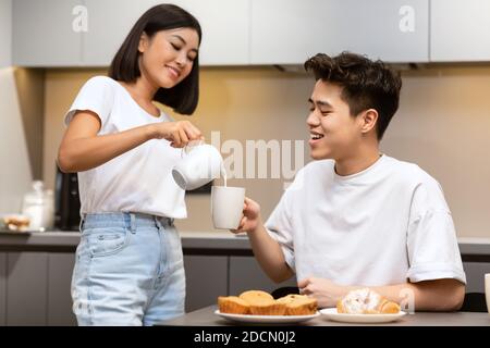 Meine Frau hat beim Frühstück in der Küche Milch zum Kaffee des Mannes hinzugefügt Stockfoto