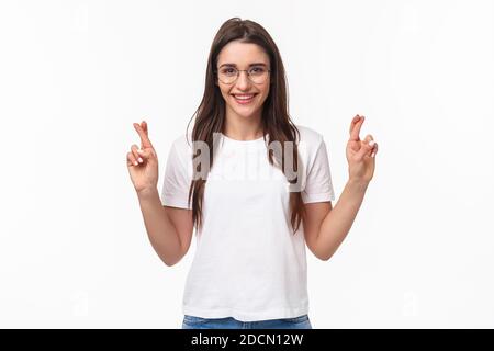 Taille-up-Porträt von optimistischen Mädchen glauben Träume wahr werden, tragen Brille und T-Shirt, Kreuzfinger Glück, machen Wunsch, beten und Stockfoto