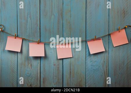 Rosa Notizpapiere hängen am Seil auf blauem rustikalem Holzhintergrund. Copyspace. Konzept von Memo-Nachrichten, To-Do-Liste Stockfoto