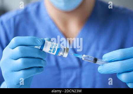 Arzt trägt Maske und Handschuhe halten Spritze unter covid 19 Impfstoff aus Fläschchen. Stockfoto