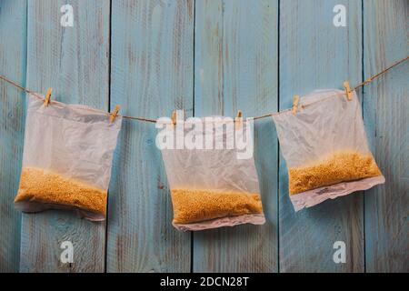 Hirse in Verpackung hängen am Seil gegen blaue rustikale Holzstruktur. Copyspace. Konzept der schnellen Getreidevorbereitung Stockfoto