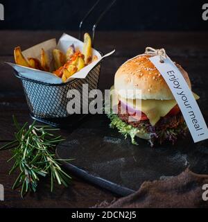 Hausgemachte vegetarische Käseburger und Pommes frites im Dunkeln Holzbrett auf einem dunkelbraunen Holztisch daneben Eine braune Leinenserviette mit einem Schild genießen Stockfoto