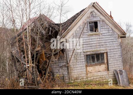 Altes verlassenes Haus, das zusammengebrochen ist. Die Fenster sind kaputt und das Dach ist eingefallen. Die Seiten sind aus Holzschindeln. Stockfoto